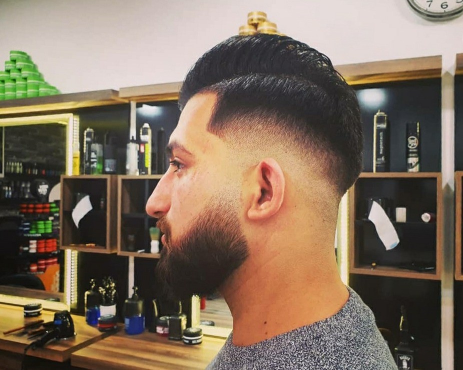 Klant van opzij met een hoge fade en een volle, strak getrimde baard, voor de productkasten