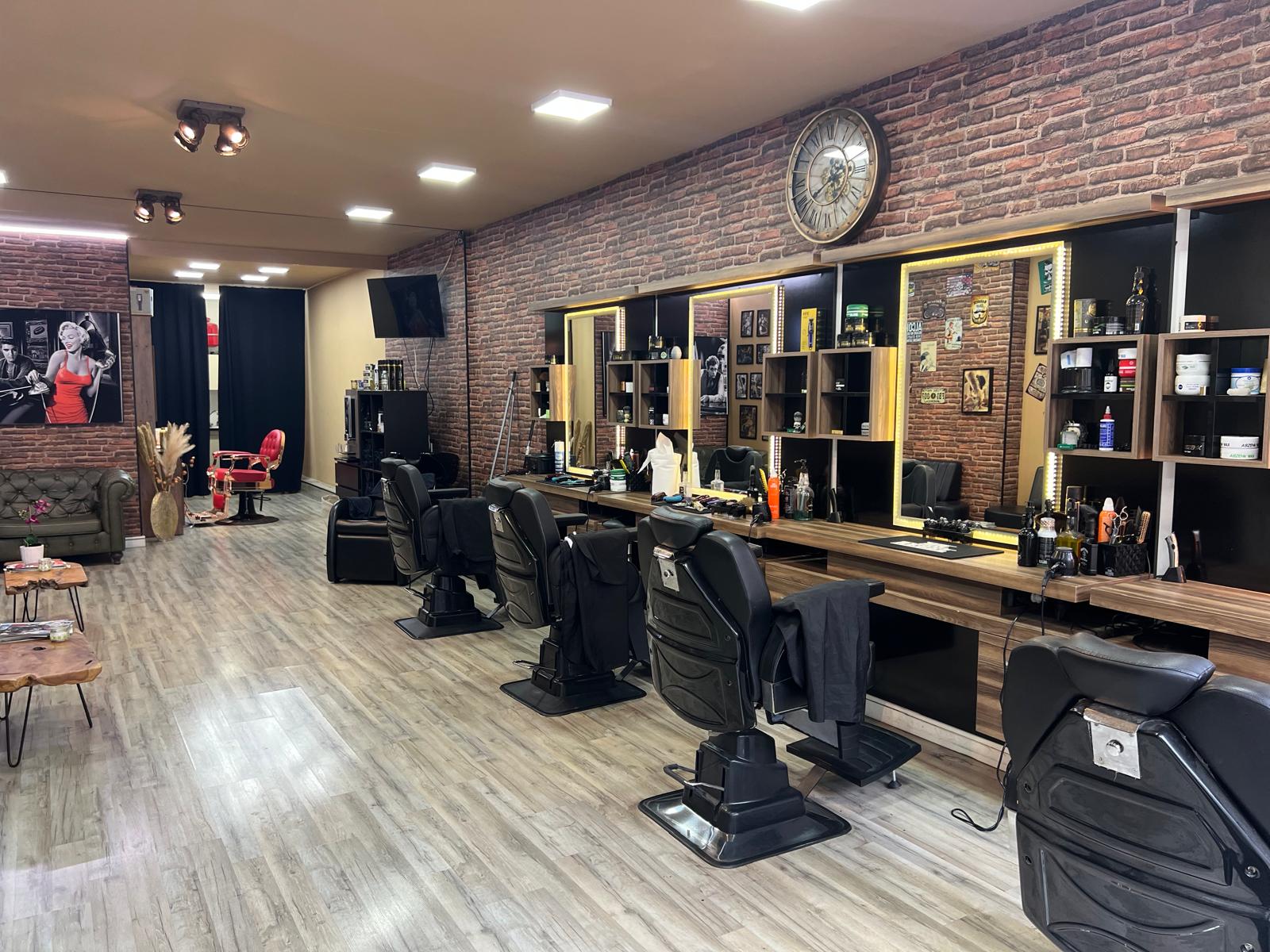 Interieur van R&A Barbershop: bakstenen muur, spiegelwand met verlichte kasten en zwarte barberstoelen